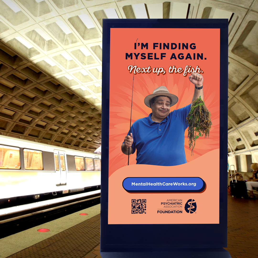 A digital ad display in a metro station. On the ad, a man is holding up his fishing rod to show the hook has only caught seaweed. Text next to him reads I'm finding myself again. Next up, the fish. mentalhealthcareworks.org. American Psychiatric Association Foundation logo.